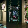 Trois écrans rectangulaires placés en position verticale, et ornés de feuillages, sont suspendus dans les airs dans une salle d'exposition. 