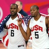 Lebron James et Kevin Durant, chacun avec l'uniforme de l'équipe américaine de basketball, célèbrent la victoire de leur équipe avec un drapeau américain sur le dos.