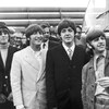 Une photo en noir et blanc des quatre membres des Beatles souriant à la caméra. 
