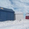 Des petites maisons peintes aux couleurs du drapeau de l'Acadie sous la neige. 