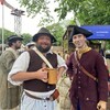 Deux hommes en costumes du 18e siècle, l'un en paysan qui tient une chope de bière à la main et l'autre en soldat avec un tricorne sur la tête.