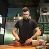 Un employé coupe un morceau de viande dans une cuisine. 