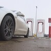 Une voiture blanche devant des bornes de recharge de véhicules électriques de la marque Tesla.