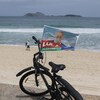 Un drapeau aux couleurs de Lula da Silva flotte sur un vélo garé sur une plage.