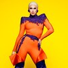 Brooke Lynn Hytes porte une tenue orange et violette et pose devant un fond jaune. 