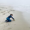 Une petite fille joue dans le sable sur le bord de l'eau, le littoral se perd dans le brouillard.