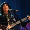 Buffy Sainte-Marie joue de la guitare devant un micro, sur scène.