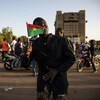 Un homme agite un drapeau du Burkina Faso au milieu d'une place publique bondée de motocyclistes. 