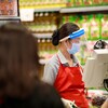 Une caissière de supermarché portant un masque, une visière et des gants.