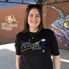 Caitlin Furlong pose pour une photo debout sur une place publique devant une murale peinte qui représente un poisson multicolore.