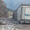 Un camion porte-conteneurs est sur la route jouchée de boue et de débris.