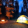 Une tente de camping dans la forêt près d'un feu.
