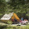 Une tente luxueuse et une famille qui pique-nique dans la forêt.
