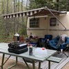 Un site de camping avec une roulotte. Des chaises et une table à picnic sont installées devant. 