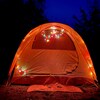 Une tente de camping orange décorée avec des lumières de Noël, le soir sur un terrain de camping d'un parc national.