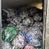 Des dizaines de sacs remplis de canettes et de bouteilles de plastique vides se trouvent dans un conteneur.