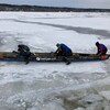 Plusieurs personnes poussent un canot sur la glace.