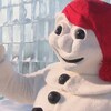 La mascotte du Carnaval de Québec, un bonhomme de neige avec un bonnet rouge sur la tête, devant des blocs de glace empilés les uns sur les autres.