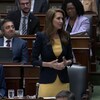 Caroline Mulroney parle en Chambre. Le ministre Calandra et quelques autres députés sourient derrière elle.