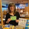 Monika Kinner qui tient une carte postale en tissus dans un magasin.