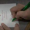 Une main écrit un message sur une carte postale. 