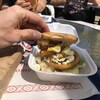 Une main montre un burger avec de la poutine à l'intérieur.