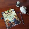 Le livret du jeu Dragons & Travellers' Tales est déposé sur une table avec un crayon et des dés.
