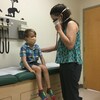 Un enfant masqué est assis sur une table d'examen médical pendant qu'un médecin l'ausculte.