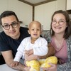 Un père et une mère sourient, avec leur enfant assis sur le comptoir de la cuisine.