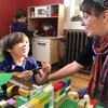 Une femme écoute un enfant, en train de jouer avec des blocs. Elle lui sourit.