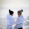 Les deux jeunes femmes sont face à face et se tiennent par les avant-bras, souriantes. Derrière elle, on voit un paysage enneigé et glacé.