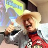 Charles Martinet, souriant, devant une affiche du Comiccon. 