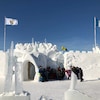 Sous un ciel bleu, des gens sont debout à côté du chateau de neige du Festival d'hiver Snowking
