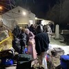 Des demandeurs d'asile font la file devant une petite cabane, le soir. 