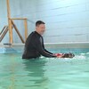 Un moniteur de natation aide un labrador à se déplacer dans une piscine intérieure.