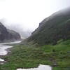 Des gens marchent sur un sentir près d'une rivière et des montagnes. 