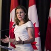 Mme Freeland parle devant des drapeaux du Canada.