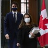 Chrystia Freeland, masquée, tenant des documents, marche suivie de Justin Trudeau, également masqué.
