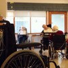 Des résidents et une employée dans un CHSLD avec, à l’avant-plan, un fauteuil roulant.