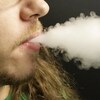 Un jeune homme fume une cigarette électronique.