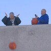 Une femme laisse tomber une citrouille à partir d'un toit alors que des gens souriant autour d'elles enregistrent le geste environnemental. 