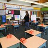 Une enseignante qui porte un couvre-visage se déplace dans une classe vide.