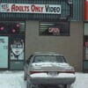 Une voiture stationnée devant un club vidéo pour adultes. 