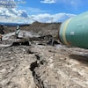 Un bout de pipeline surplombe un sol sec et dénudé traversé par une faille.