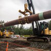 De grands tronçons de tuyaux sont mis en terre à l'aide de machinerie lourde.