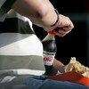 Un homme obèse ouvre une bouteille de coke.