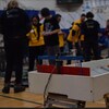 Des jeunes à l'arrière-plan déploient leurs robots alors qu'on en voit un à l'avant-plan.  