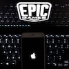 Le logo d'Apple affiché sur un téléphone, qui est déposé sur un clavier d'ordinateur dont l'écran affiche le logo d'Epic Games. 