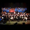 De nombreux chanteurs d'une chorale et des musiciens d'un orchestre symphonique en prestation sur scène.