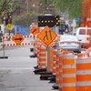 Des cônes orange, des panneaux et une flèche clignotante détournent la circulation près d'un chantier de construction.